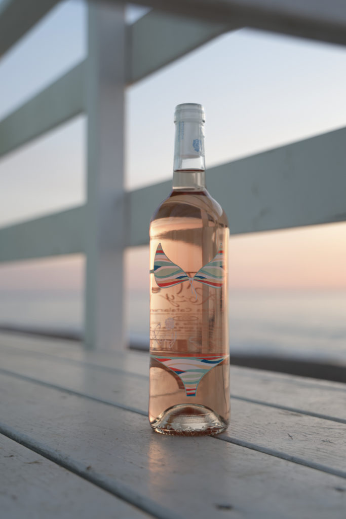 Bouteille de vin rosé Rozy 2024 « Vague de Fraîcheur » sur fond de vagues et de sable